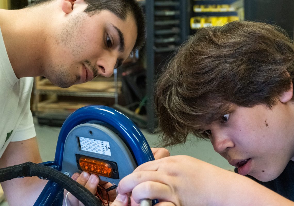 Nittany Motorsports team members work to secure a marker and brake light to the chassis of the car. One works to hold the pieces in place, while the other installs fastening hardware.