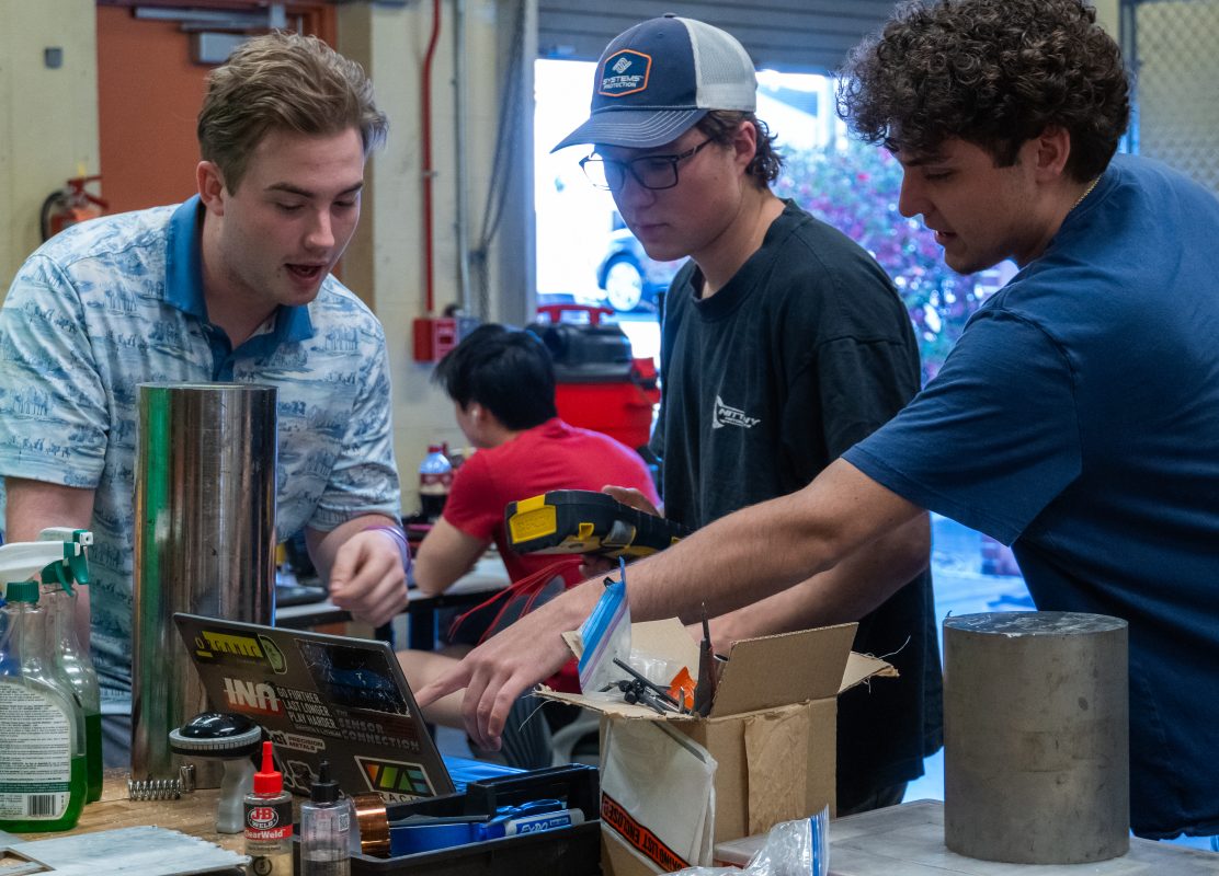 Nittany Motorsports team members review a connector's pinout before crimping pins on wires and pinning connectors. The pinout is determined by the designer of the circuit board based on various electrical and physical constraints.